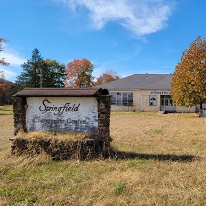 Single story brick building in disrepair with faded stone and wood sign "Springfield Community Center"