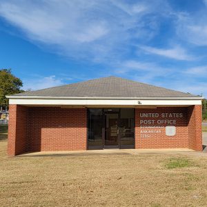 Single story red brick post office building with parking lot