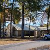 Single story beige stone church building with parking lot surrounded by trees