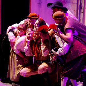 Group of actors huddled on a stage lit in purple