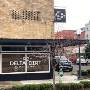 Multistory orange brick building with "Delta Dirt Distillery" on window glass