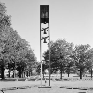 A tower of bells with gravestones and trees behind it