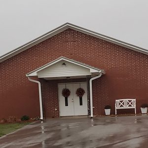 Single story red brick church building with parking lot