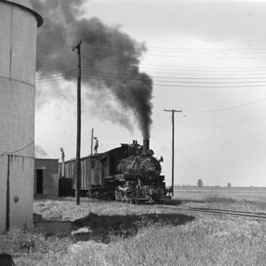 Train emitting plume of smoke going by buildings on its right