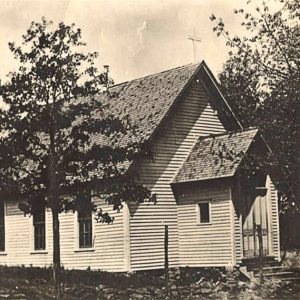 White wooden church building with cross on top and trees around