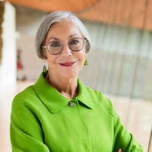 Older white woman smiling in green suit and glasses with earrings