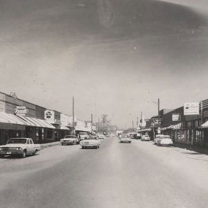 Downtown street scene with tightly bunched storefronts and cars parked and on the road