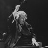 Older white woman in glasses holding a baton over her head