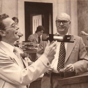 One white man giving another white man a present of a pen holder