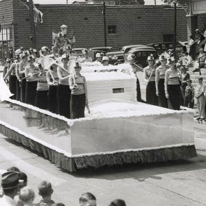 Parade float featuring uniformed people holding picks and shovels on city street with onlookers