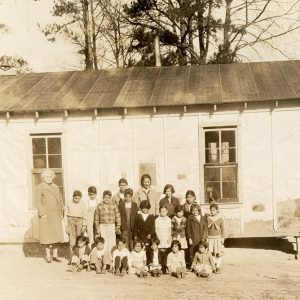 A woman and her students posing together outside a small school house at Bauxite