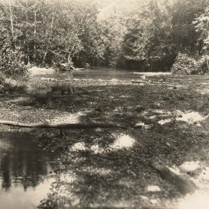 Old car crossing creek bed in wooded area