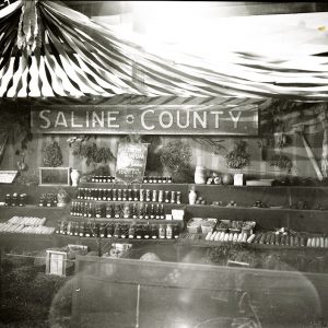 Canned food and pottery on shelves under a sign saying "Saline County"