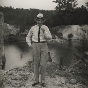 White man in hat standing before body of water