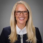 White woman in white-collared suit and glasses