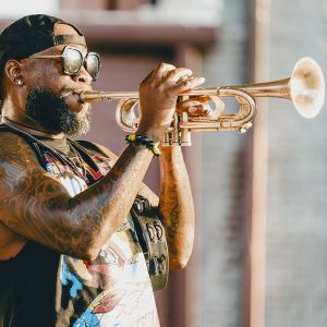 African American man playing trumpet in sunglasses and backwards cap