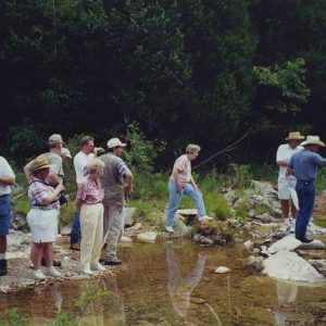 Group of white people in casual clothing and hats standing on a river bank