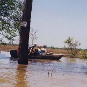 people in a fishing boat with a motor in brown water next to land