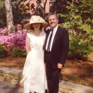 White man in suit and white woman in hat with flowers on it and white dress