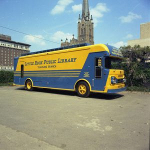 Blue and yellow bus parked in lot with various city buildings in background