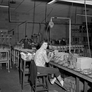 Woman in short-sleeved shirt and pants sitting at factory machinery