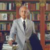 White man in suit and tie standing before wooden bookshelves