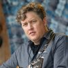 closeup of white man in button down shirt holding a guitar