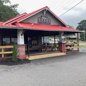 BBQ restaurant with patio featuring wooden picnic tables and red metal roof