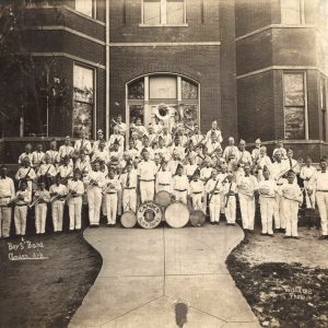 boys posing in white clothes and holding instruments in front of a brick building