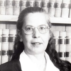 White woman in judicial robes and glasses standing in front of bookcase