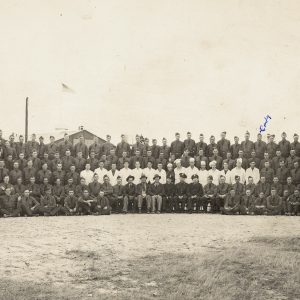 Large group of white men posing for a group photo with wooden buildings in background