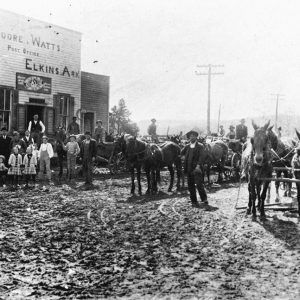 People and teams of horses in front of a wooden building