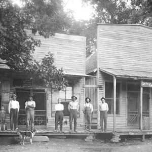 white men and boys and a dog in front of wooden building "fresh groceries"