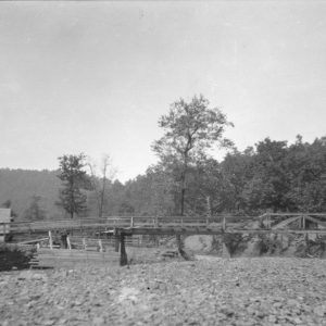 Small bridge spanning small creek with stone building on one side and wooded area on the other