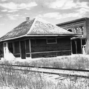 Small wooden train depot building in front of larger brick building