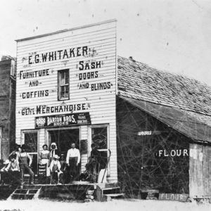 Group of white people standing on porch in front of wooden store buiding