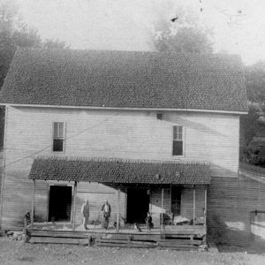 Men standing on porch of large multistory wooden building