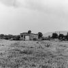 two buildings and some vehicles on grassy land with hills in the distance