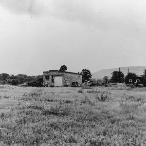 two buildings and some vehicles on grassy land with hills in the distance