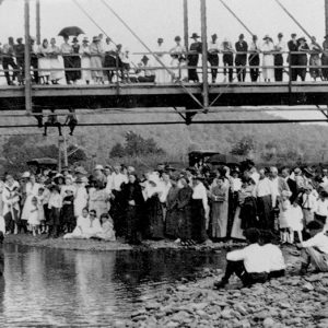 People standing on and under a bridge over a waterway where a man and woman are standing in the water