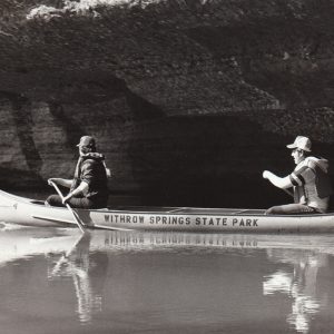 two men in a canoe in live jackets and hats rowing a canoe that says "Withrow Springs State Park" on the side