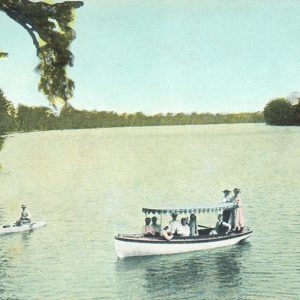 people in a boat and two canoes on a lake with wooded banks