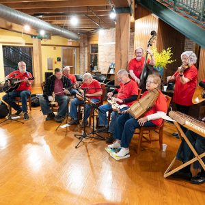 Group of white men and women playing musical instruments next to stairwell