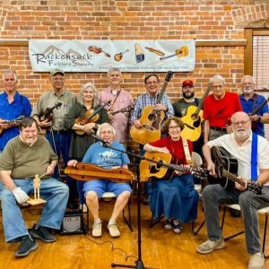 Group of white men and women with musical instruments posing in front of brick wall