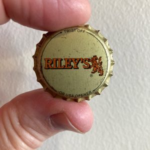 Fingers holding a bottle cap "Riley's"