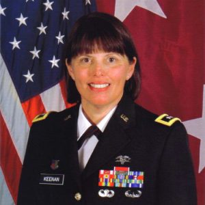 White woman in military uniform smiling with flags behind her