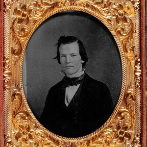 Gold colored frame with floral patters and a centered oval shaped black and white portrait of a young white man wearing a suit