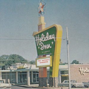 Single-story building with green and yellow sign on street "The Nation's Innkeeper"