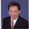 Portrait photograph of white man with brown hair in suit and tie