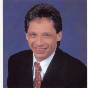 Portrait photograph of white man with brown hair in suit and tie